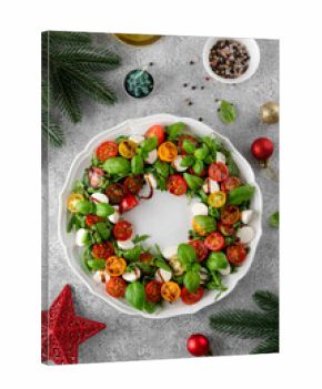 Christmas wreath Caprese salad with arugula, mozzarella, cherry tomatoes, fresh basil and balsamic glaze on a white plate on a gray concrete background. Top view.