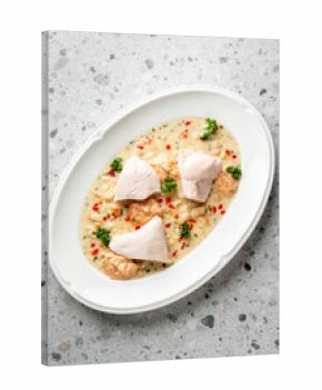Poached white fish in a creamy sauce with vegetables & herbs, served in an elegant white oval dish on a speckled grey stone background
