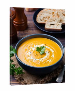 Pumpkin and carrot soup with cream and parsley on dark wooden background.