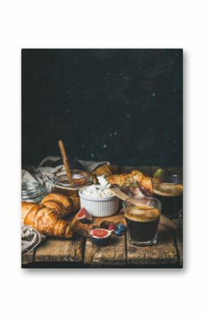 Breakfast with croissants, ricotta cheese, figs, fresh berries, prosciutto meat, honey and espresso coffee on rustic wooden table, dark blue plywood wall background, selective focus, copy space