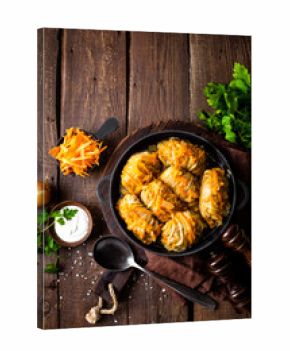 Cabbage rolls stewed with meat and vegetables in pan on dark wooden background, top view
