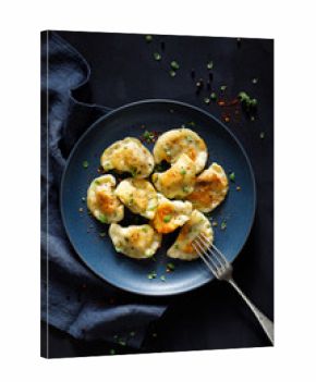 Dumplings, pierogi stuffed with meat sprinkled with fresh herbs on a blue plate, top view, black background. Traditional food in Poland