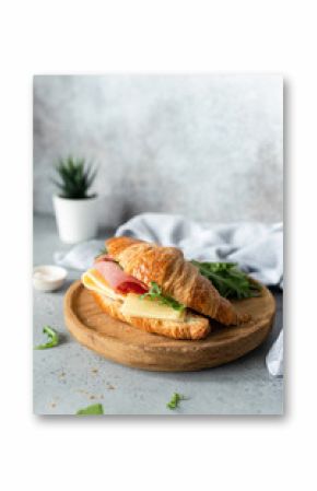 Croissant sandwich with cheese, ham and arugula on wooden cutting board, gray concrete background. Selective focus. Tasty breakfast sandwich or snack
