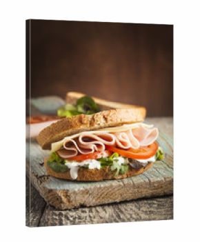 Tasty sandwich with ham, cheese, tomato and lettuce on wooden background