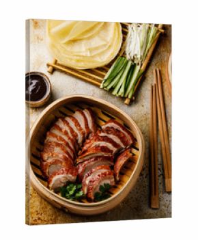Sliced Peking Duck in bamboo steamer served with fresh cucumber, onion, Hoysin sauce and roasted wheaten pancakes on metal background