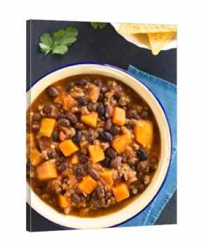 Homemade chili con carne with mincemeat, red and black beans, tomato sauce and pumpkin with tortilla chips on the side, photographed overhead on slate (Selective Focus on the chili)