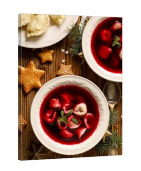 Christmas beetroot soup, borscht with small dumplings with mushroom filling in a ceramic bowl on a wooden table, top view.  Traditional Christmas eve dish in Poland. 