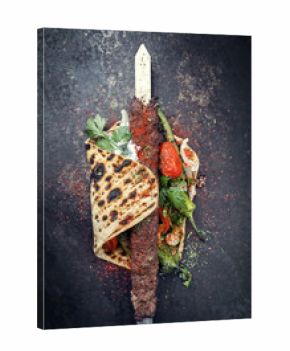 Traditional Adana kebap on a skewer with tomato and yogurt on a flatbread