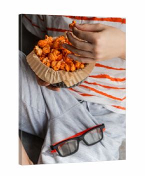 Close-up of a boy with a pair of 3D glasses on his lap eating a bowl of homemade cheese popcorn