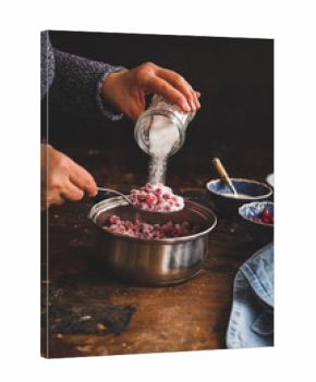 Red berries jam. Person making jam, jelly, confiture over rustic wooden table.