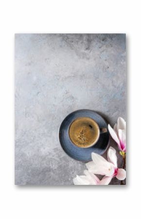 Blue cup of black espresso coffee and spring flowers magnolia branches over grey texture background. Top view, copy space. Spring greeting card
