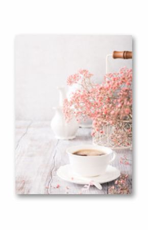 White cup of coffee with pink flowers on old white wooden background with copy space.