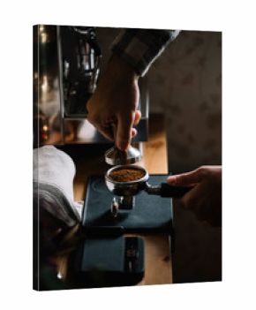 The process of making coffee step by step. Man tamping freshly ground coffee beans in a portafilter on a working wooden table