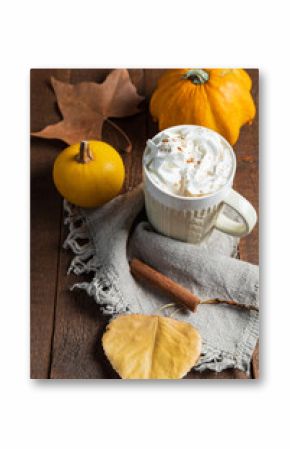 Spicy pumpkin latte with cinnamon and autumn leaves on wooden background