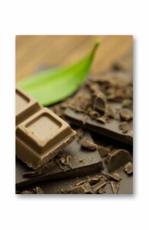 milk chocolate square is resting on dark chocolate fragments beside green leaf in macro photography