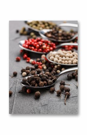 Colorful peppers in spoon on black table - cubeb, pink, green and white closeup. Spices. Selective focus