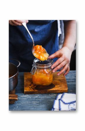 Home canning ham. Housewife filling peach, melon, pineapple and apricot jam into a glass. Rustic blue style.