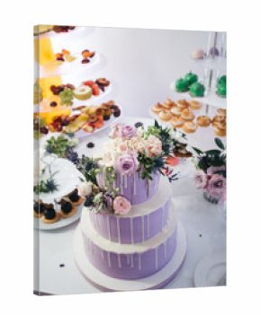 Front view of beautiful decorated with rose flowers wedding cake in dim lavender color, yummy desserts and cupcakes on candy buffet. Complicated delicious french recipe for pro. Concept of calories.