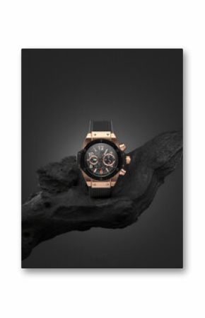 Beautiful gold men's watch with a black strap on a wooden stand, on a gray background. Beautiful gold watch. A luxury brand watch