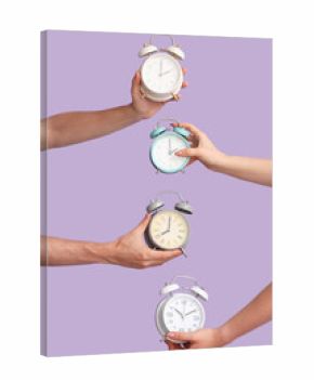 Hands holding different alarm clocks on lilac background
