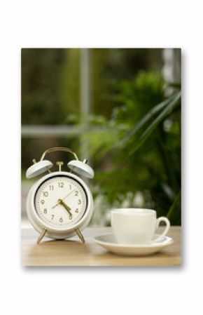 A cup of coffee, an alarm clock on the table near the window. Coffee break time.