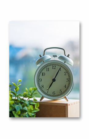 The white vintage alarm clock showing time 7 am in the morning next to the window under morning light.