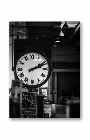 Old fashioned vintage big industry factory clock hanging with roman numerals in abandoned building no workers. Industrial workshop clocking off time deserted retro design manufacturing black and white
