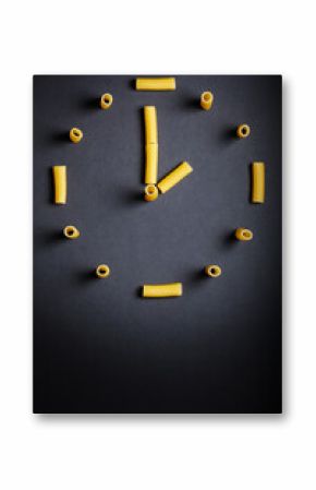 Uncooked pasta designed in clock shape on dark background. vertical photo