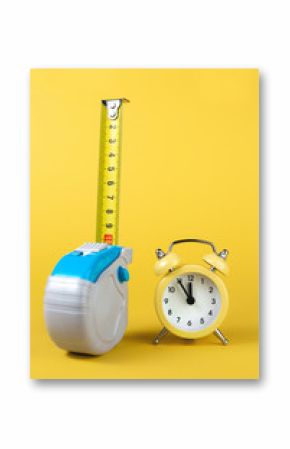 Measuring tape and alarm clock isolated over yellow bakground. Carpenter and Construct concept.