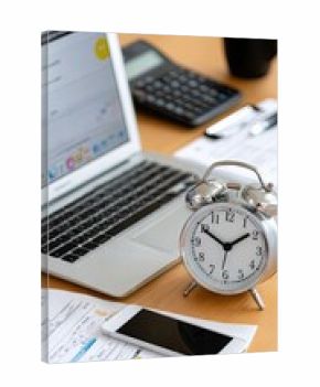 A cozy home office features a black alarm clock on an organized desk with graphic design tools, vibrant natural light flooding in, and a pop of green from a plant.