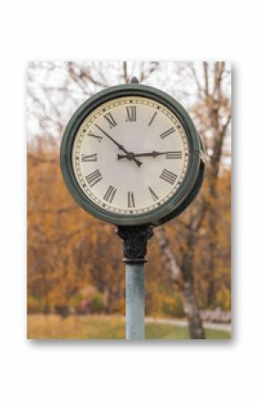 Vintage clock stands tall in a park surrounded by autumn foliage during daytime in a serene setting