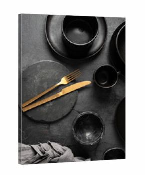 Top view of black ceramic collection, different bowls, plates, mugs and gold cutlery with napkin. .