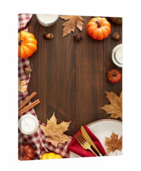 Autumn-themed decor concept. Top view vertical shot of plate, cutlery, napkin, tablecloth, pumpkins, cinnamon sticks, candle, dry leaves on brown wooden table background with space for advert or text