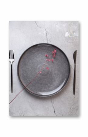 Top-down view of a table with an elegant and minimalist composition. A grey ceramic plate with a stylized pink flower, accompanied by modern cutlery and a glass cup on a concrete surface. Copy space. 