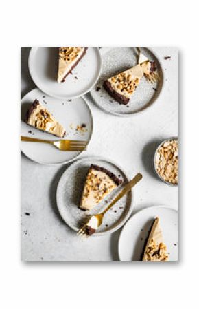 Top view of several slices of cheesecake with nuts on plates, alongside a bowl of peanuts and golden forks.
