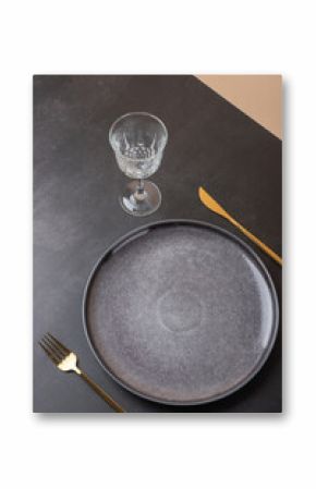 Top view of a gray plate with golden cutlery and crystal glass on dark and nude stone background. Sophisticated aesthetics. Copy space. Concept of elegant table and modern decoration