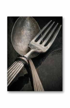 Ancient worn vintage cutlery on the black background. Crossed black metal spoon and fork in dark tone, Highlighting its texture and design, use it as your Space for text, Design, Wallpaper and Poster,