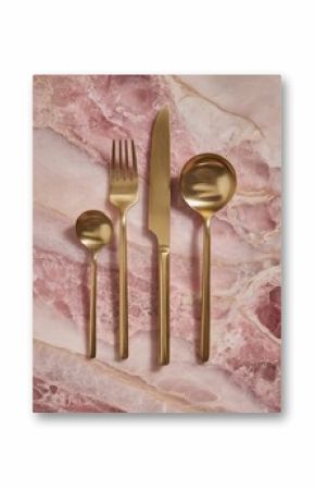 Gold cutlery set (fork, knife, spoon, teaspoon) arranged on a pink marble background.  The metallic finish is matte