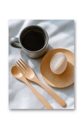 Close-up of a white ceramic coffee mug filled with black coffee on a white cloth background with wooden cutlery and a soft-boiled egg on a wooden plate for breakfast or morning coffee break beverage
