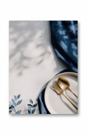 Minimal festive table setting with white plate and golden cutlery on blue silk fabric ideal for christmas dinner designs, seasonal styling and elegant holiday presentations