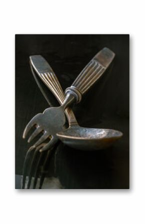Ancient worn vintage cutlery on the black background. Crossed black metal spoon and fork in dark tone, Highlighting its texture and design, use it as your Space for text, Design, Wallpaper and Poster.