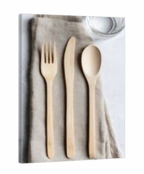 Minimalist composition featuring natural light wood cutlery on a beige linen napkin, with a glass of water blurred in the background, all on a textured white surface