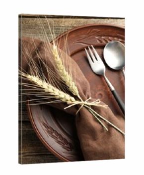 Wheat spikes, plate and cutlery on wooden table, top view