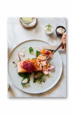 Woman eating grilled salmon with salad at marble table