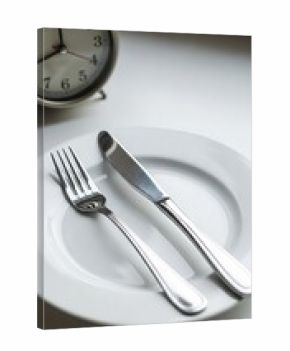 Empty plate with cutlery and alarm clock