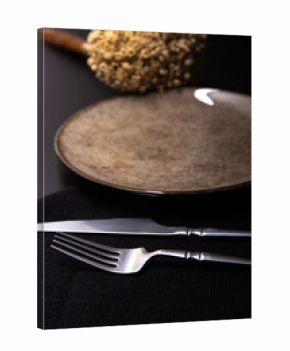 Table set in detail, with napkin, beautiful plate and beautiful cutlery, on a dark surface with small flowers, selective focus.