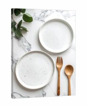 Two plates, wooden cutlery & eucalyptus on marble surface