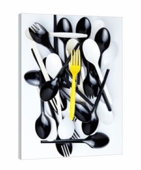 A yellow plastic fork on top of a stack of black and white cutlery