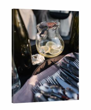 Elegant table setup with a glass pitcher filled with lemon slices, surrounded by wine bottles. Neatly arranged cutlery on a napkin, with a decorative rope detail. Perfect for a sophisticated outdoor