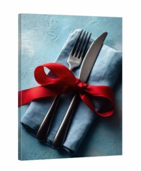 Elegant dining setting with silverware wrapped in red ribbon on blue napkin